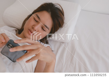 Asian woman browsing and checking social media feed in her mobile phone, can not sleep. Asian woman browsing and checking social media feed in her mobile phone, can not sleep. 111050235
