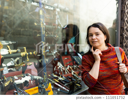 Woman tourist, standing near the window of a souvenir shop, examines the goods 111051732