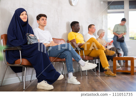 Girl in traditional veil, along with other people of different nationalities, is waiting for a specialist sitting on a chair in hall 111051735
