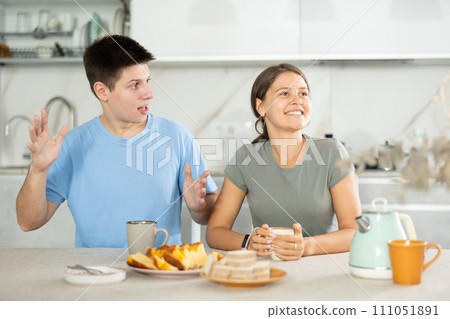 Cheerful young couple talking and laughing while having coffee at home Cheerful young couple talking and laughing while having coffee at home 111051891