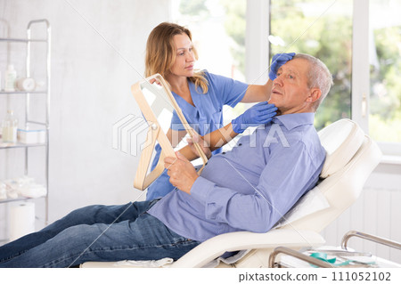 Female cosmetologist explaining facial procedure to elderly male patient Female cosmetologist explaining facial procedure to elderly male patient 111052102
