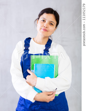 Young female mechanic in blue overalls holding workbooks 111052179