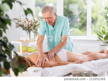 Skilled old masseur conducting back massage for woman client 111052368