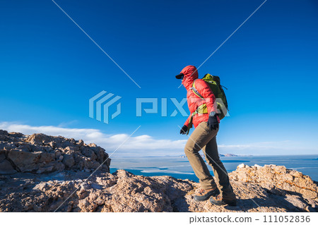 Woman hiker climbing to mountain top cliff edge at lakeside 111052836