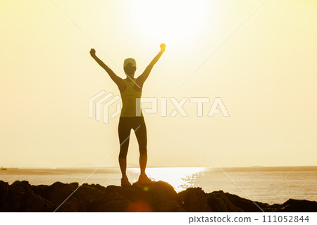 Woman open arms to sunrise at seaside rocks 111052844