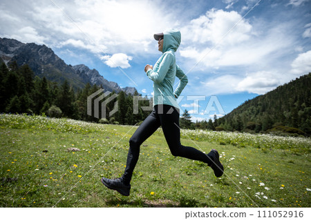 Woman trail runner cross country running in high altitude flowering mountains 111052916