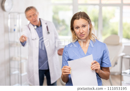 Upset middle-aged nurse standing with her back to angry doctor 111053195