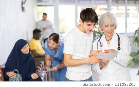 Elderly woman doctor gives document to teenager guy for signing Elderly woman doctor gives document to teenager guy for signing 111053203