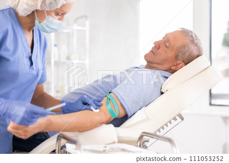 Senior man lying on couch, getting intravenous injection in medical office 111053252