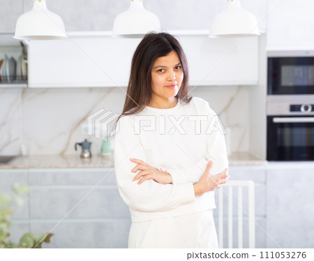 Smiling young brunette in white clothes standing in home kitchen 111053276