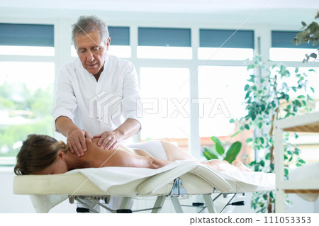 Skilled old masseur conducting back massage for woman client Skilled old masseur conducting back massage for woman client 111053353