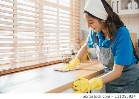 Asian woman in yellow gloves cleans wooden kitchen counter with liquid spray ensuring hygiene. Housekeeping service focusing on home cleanliness. Clean disinfect home care. maid household job. Asian woman in yellow gloves cleans wooden kitchen counter with liquid spray ensuring hygiene. Housekeeping service focusing on home cleanliness. Clean disinfect home care. maid household job. 111053924