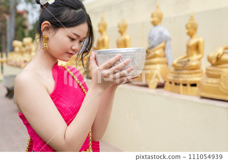 Beautiful Thai woman wearing Thai costume bathes a Buddha statue on Songkran Day. Beautiful Thai woman wearing Thai costume bathes a Buddha statue on Songkran Day. 111054939