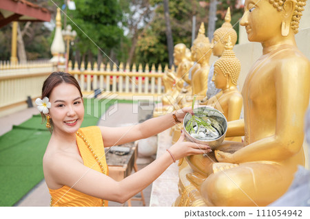 Beautiful Thai woman wearing Thai costume bathes a Buddha statue on Songkran Day. 111054942