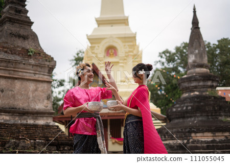 Young Thai couple wearing Thai costumes playing in the water during Songkran in the temple 111055045