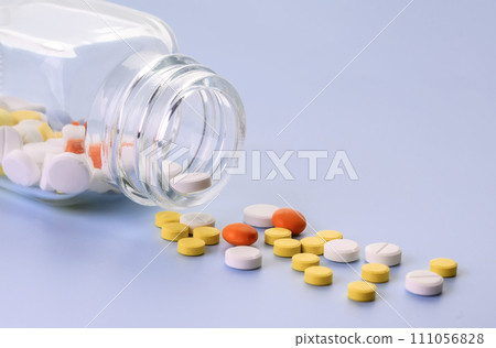 Multicolored Pills spilling out from transparent glass medicine bottle. Copy space Multicolored Pills spilling out from transparent glass medicine bottle. Copy space 111056828