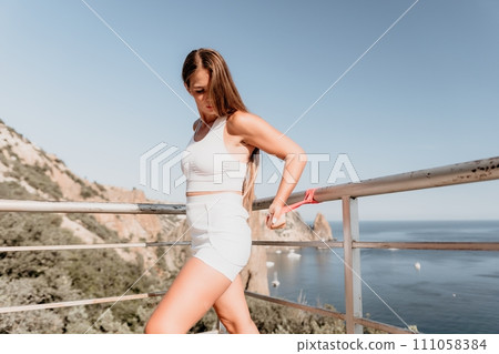 Woman sea fitness. Happy woman with long hair, fitness instructor in white doing stretching and pilates with ribbons in park near the sea. Female fitness yoga routine concept. Healthy lifestyle. Woman sea fitness. Happy woman with long hair, fitness instructor in white doing stretching and pilates with ribbons in park near the sea. Female fitness yoga routine concept. Healthy lifestyle. 111058384