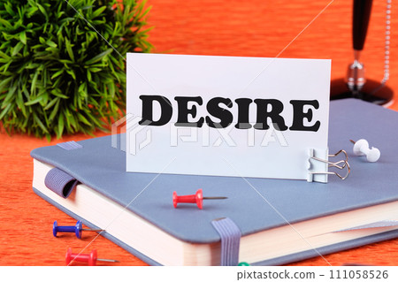 Desire text concept. DESIRE word, text written on a business card standing with a clip on a diary, a notebook on an orange background Desire text concept. DESIRE word, text written on a business card standing with a clip on a diary, a notebook on an orange background 111058526