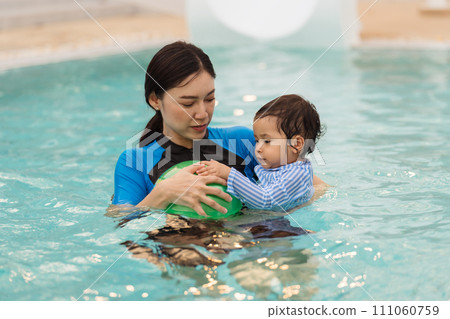 happy mother holding baby in her arms while playing ball in swimming pool 111060759