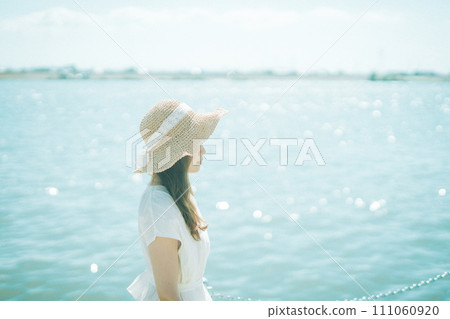 一個穿著白色洋裝、戴著草帽的女人看著大海 111060920