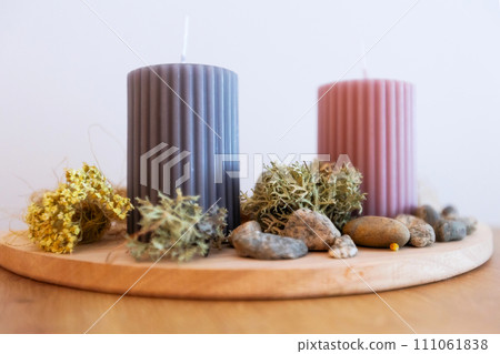Two candles on wooden holder, stones and moss 111061838