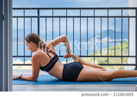 Fitness woman in sportswear stretching legs on the mat at the balcony. Fitness woman in sportswear stretching legs on the mat at the balcony. 111063095