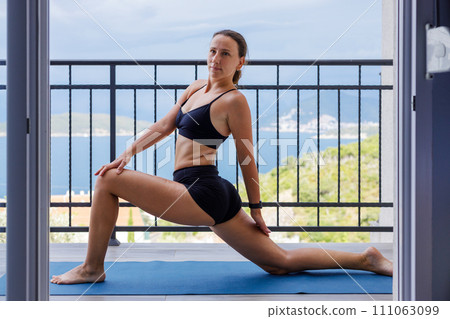 Yogi woman in sportswear stretching legs on the mat at the balcony Yogi woman in sportswear stretching legs on the mat at the balcony 111063099