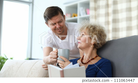 Adult son serves cup tea to an elderly mother 111063447