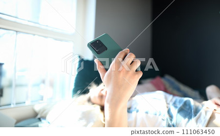 Woman lying bed and looking at smartphone screen 111063450