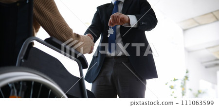 Man in suit passes house keys to disabled person 111063599