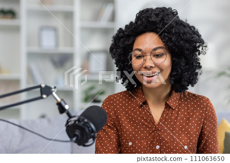 Cheerful young woman podcasting with microphone at home, expressing positivity and confidence in a cozy interior setting. Cheerful young woman podcasting with microphone at home, expressing positivity and confidence in a cozy interior setting. 111063650