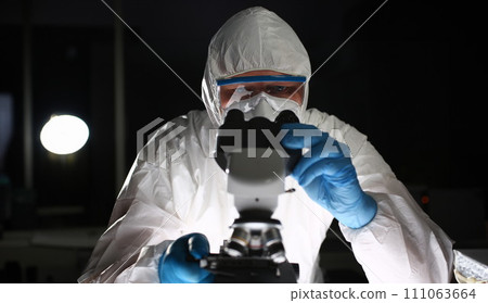 Man in protective suit looks through microscope 111063664