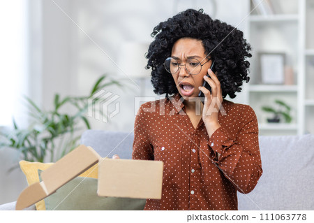 Worried young woman with curly hair on phone, looking at an open package, expressing confusion and dissatisfaction at home. Worried young woman with curly hair on phone, looking at an open package, expressing confusion and dissatisfaction at home. 111063778