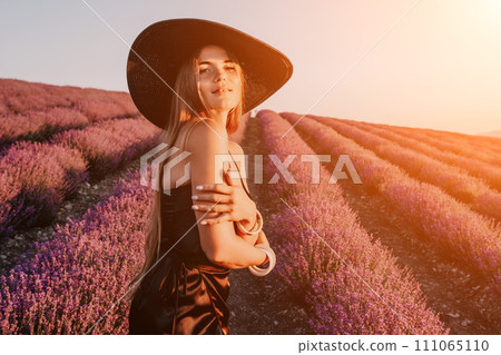 Woman lavender field. Happy carefree woman in black dress and hat with large brim walking in a lavender field during sunset. Perfect for inspirational and warm concepts in travel and wanderlust. 111065110