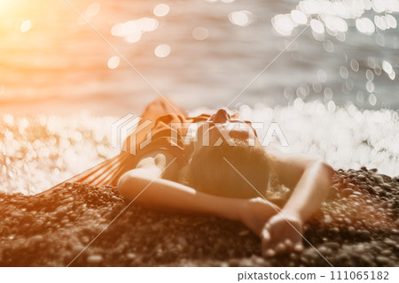 Woman in red dress on sea. Side view a Young beautiful sensual woman in a red long dress posing on the beach near sea on sunset. Girl on the nature on blue sky background. Fashion photo. 111065182