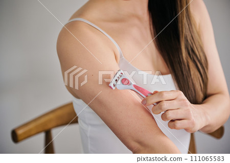 A woman in her 30s shaving her arm hair with a women's razor A woman in her 30s shaving her arm hair with a women's razor 111065583
