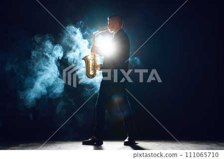 Musician with saxophone performing piece on stage with smoke. Backlit creating silhouette effect. Instrumental music. Musician with saxophone performing piece on stage with smoke. Backlit creating silhouette effect. Instrumental music. 111065710