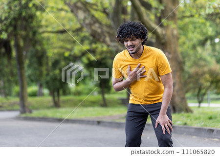 Young man in yellow t-shirt feeling chest pain while walking in park, expressing discomfort and health issue concept Young man in yellow t-shirt feeling chest pain while walking in park, expressing discomfort and health issue concept 111065820