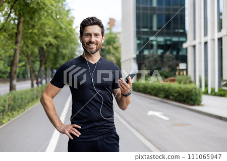 Smiling man with earphones holding smartphone, ready for jogging in urban setting, conveying health and positivity. Smiling man with earphones holding smartphone, ready for jogging in urban setting, conveying health and positivity. 111065947