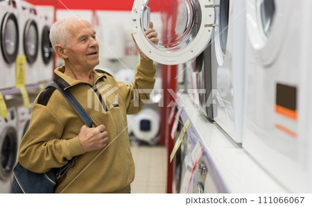 Elderly man choosing washing machine in showroom of electrical appliance store 111066067