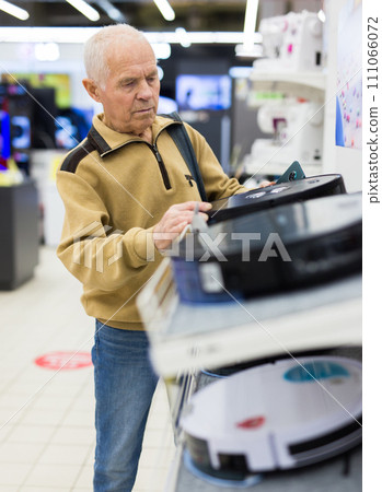 Senor man pensioner buying Robotic vacuum cleaner in showroom of electrical appliance store 111066072