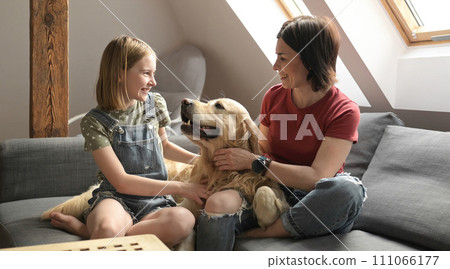 Pretty girl and preteen child family petting golden retriever dog sitting on sofa. Mother and daughter with purebred pet doggy at home smiling Pretty girl and preteen child family petting golden retriever dog sitting on sofa. Mother and daughter with purebred pet doggy at home smiling 111066177