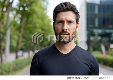 Confident adult man with stubble in urban setting. Casual attire, focused expression, blurred city background. Concept of modern lifestyle. 111066448