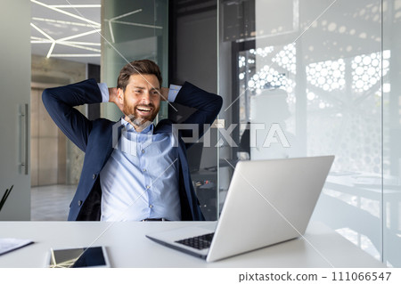 Relaxed businessman with hands behind head smiling in modern office, enjoying success and comfort, corporate well-being. Relaxed businessman with hands behind head smiling in modern office, enjoying success and comfort, corporate well-being. 111066547