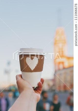 paper cup of coffee with carved white heart in women's hand on Nevsky Prospekt in St. Petersburg on sunset 111066678