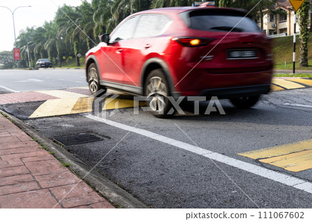 Car slowing down at speed bump or road hump painted in yellow and black stripe. Motion blur intended. Car slowing down at speed bump or road hump painted in yellow and black stripe. Motion blur intended. 111067602
