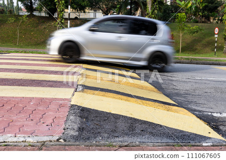 Car slowing down at speed bump or road hump painted in yellow and black stripe. Motion blur intended. Car slowing down at speed bump or road hump painted in yellow and black stripe. Motion blur intended. 111067605