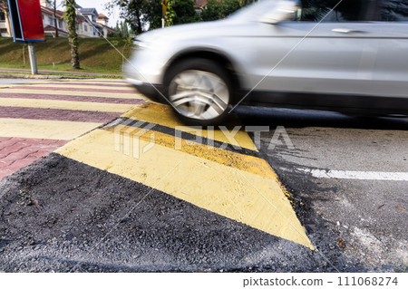 Car slowing down at speed bump or road hump painted in yellow and black stripe. Motion blur intended. Car slowing down at speed bump or road hump painted in yellow and black stripe. Motion blur intended. 111068274