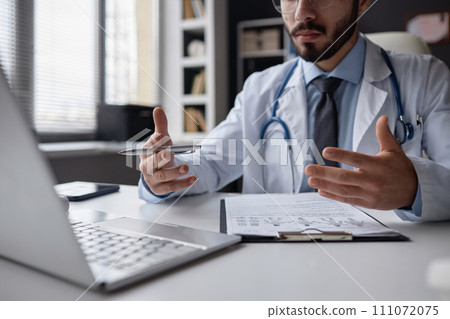 Cropped shot of unrecognizable male general practitioner talking to patient during online consultation using laptop sitting at desk in hospital 111072075