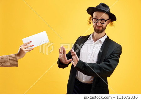 Jewish man refuses envelope with money held by someone's hand against warm yellow studio background. Business. Jewish man refuses envelope with money held by someone's hand against warm yellow studio background. Business. 111072330